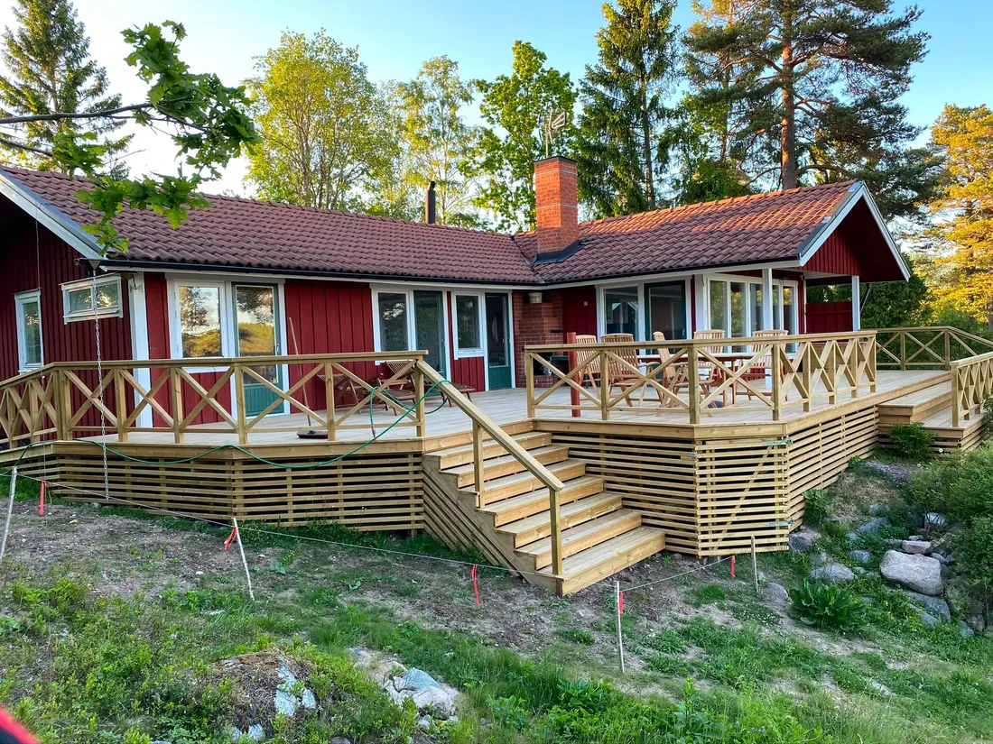Stor altan med räcke vid röd stuga i naturen