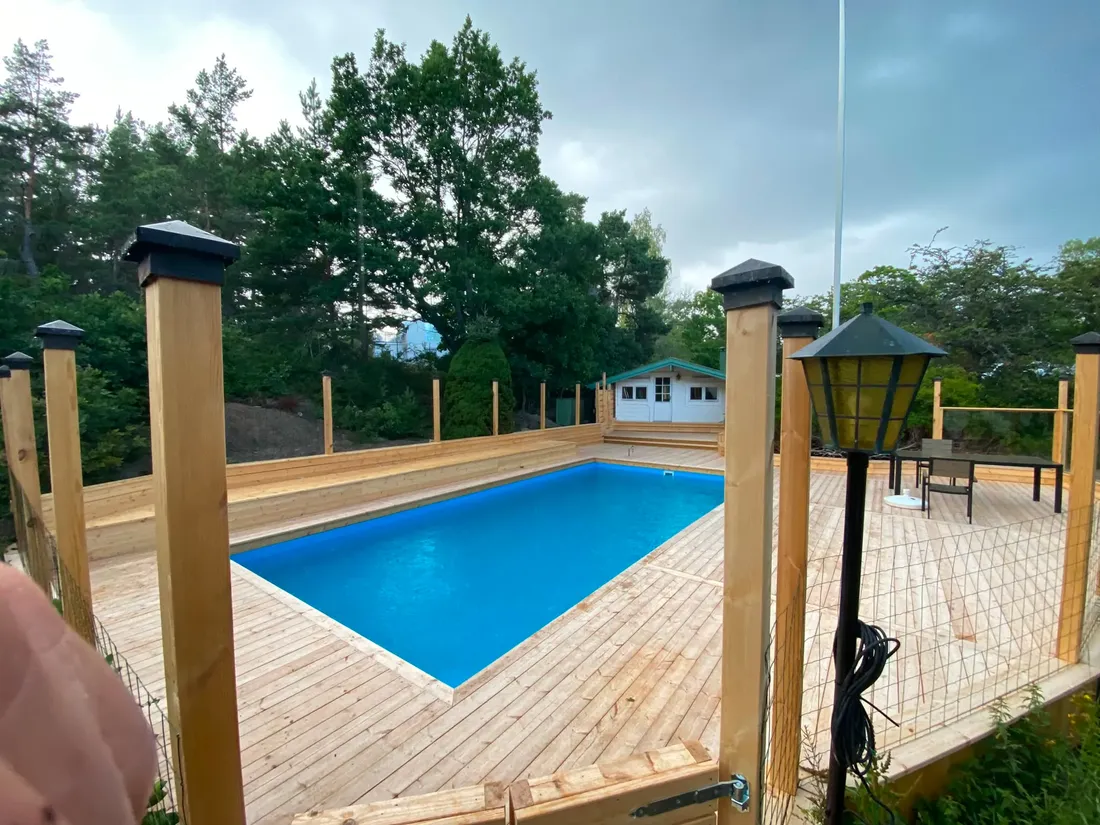 Trädäck runt pool med stolpar och lyktor i grönskan