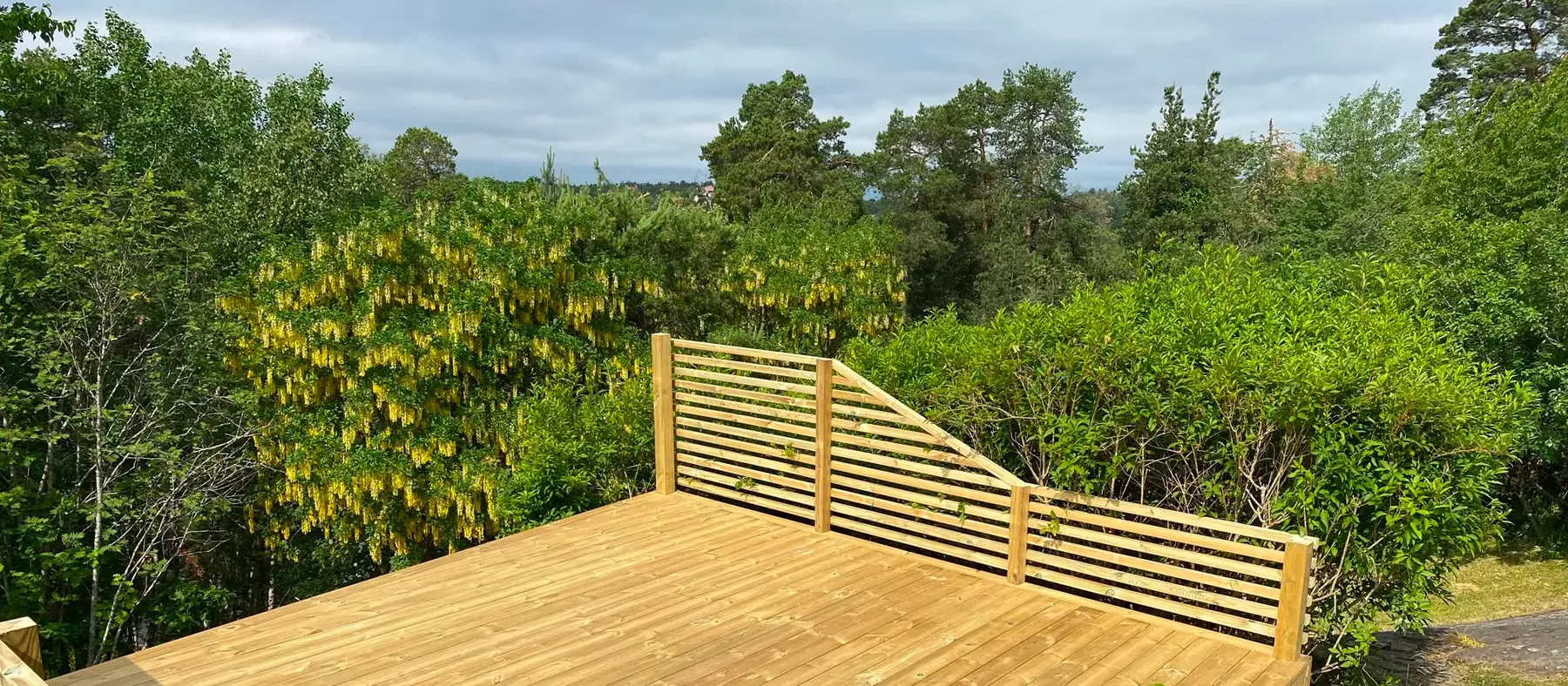 Stort trädäck vid villa i sommargrönska